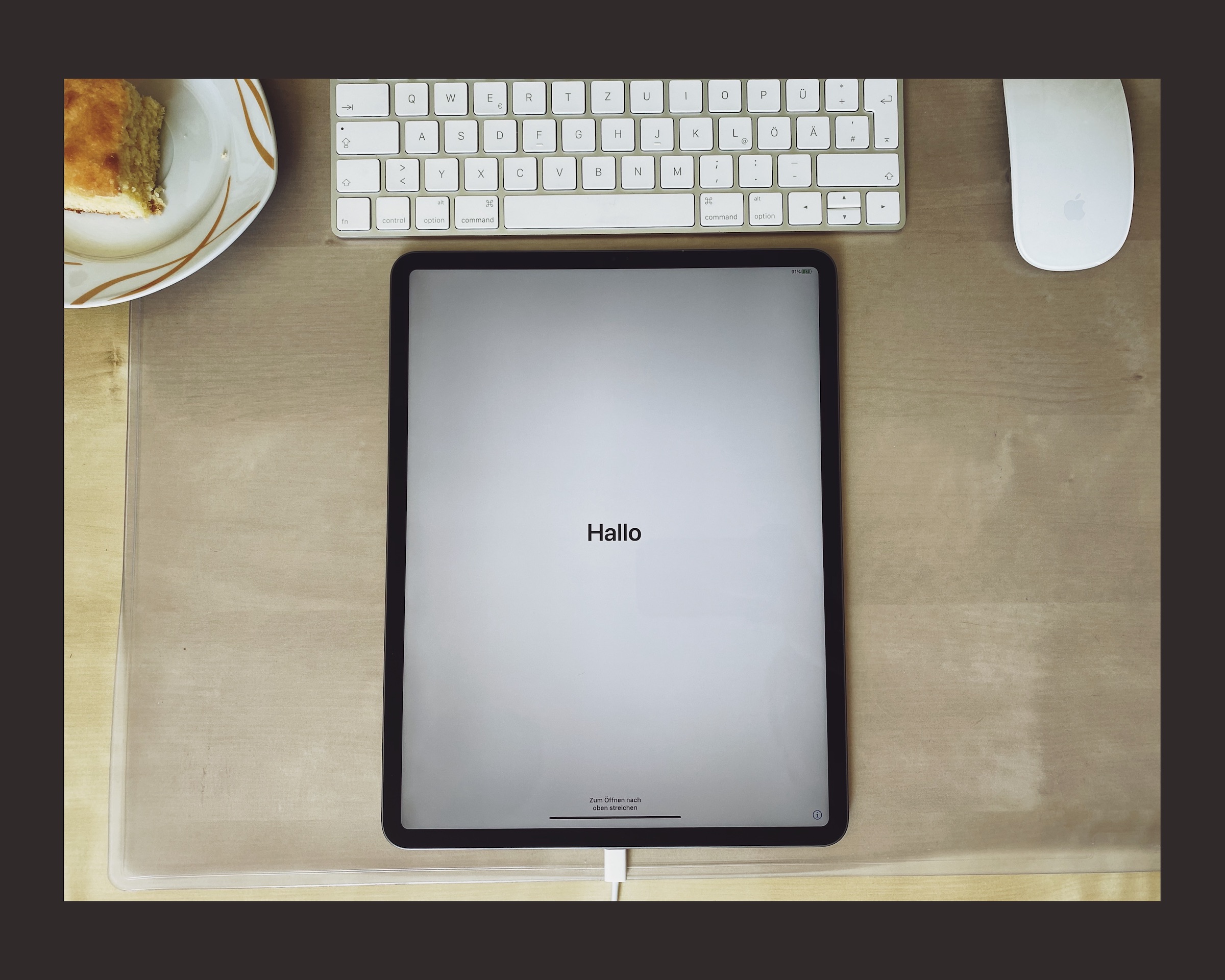 An iPad on a table displaying Hello screen on setup, next to a cake, a keyboard and a mouse